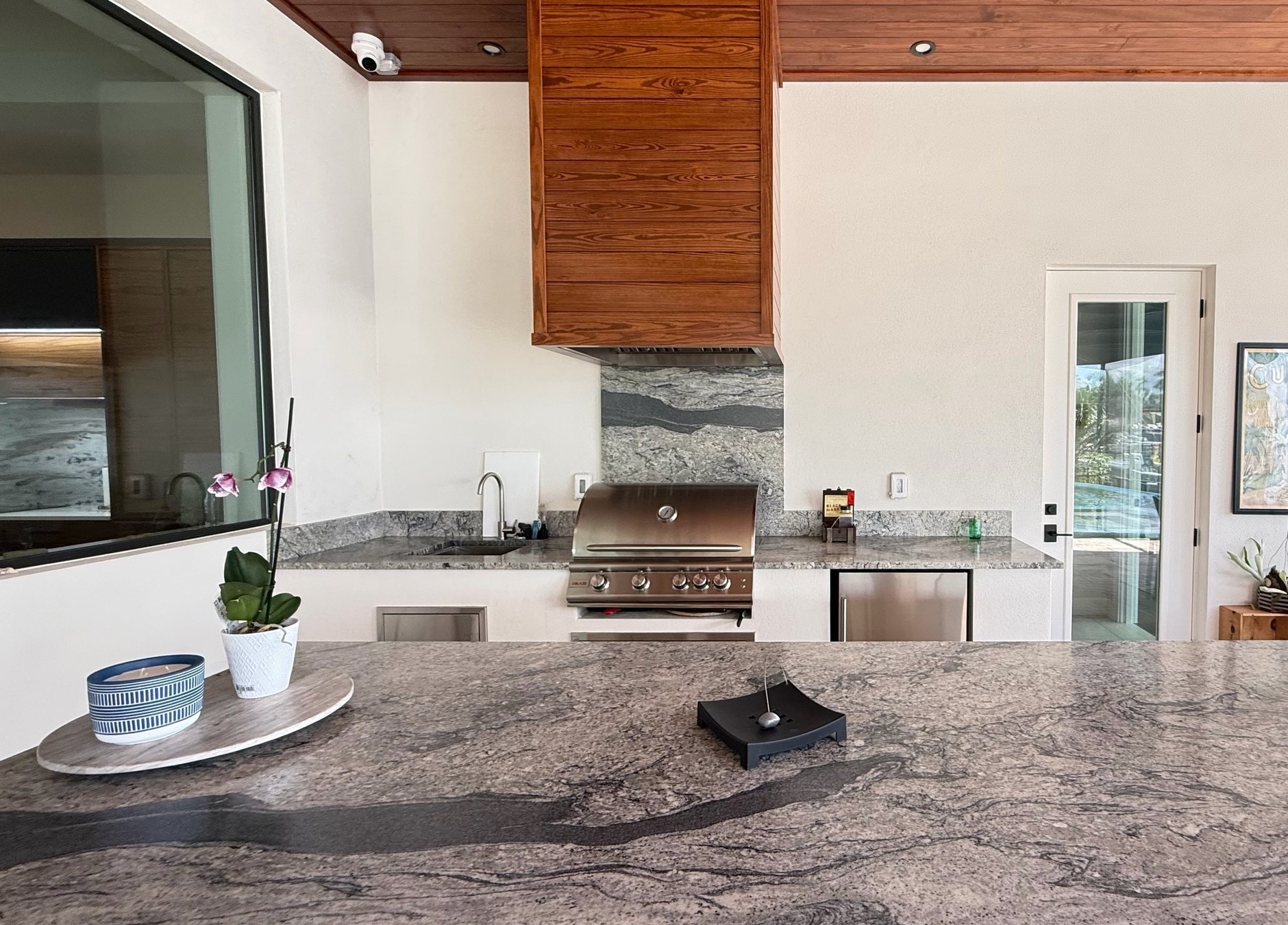 Outdoor kitchen with a stone counter, grill and cedar hood on a covered lanai